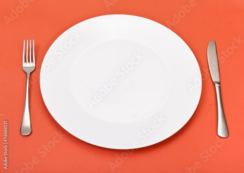 above view of porcelain plate, fork, knife on red
