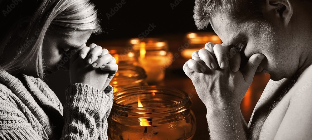 Praying man and woman with candles on background.