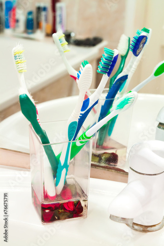Five colorful toothbrushes in a water glass