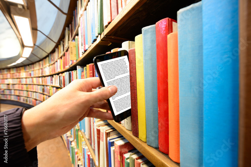 Hand picking a tablet computer out of bookshelf in library