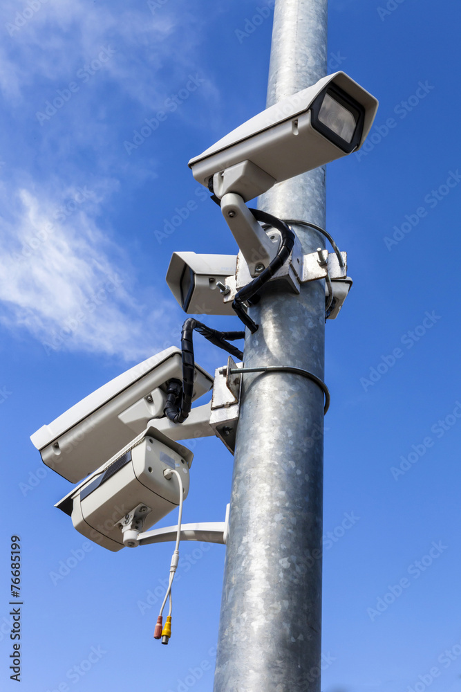 four cctv installed on metal light pole, vertical photo on blue