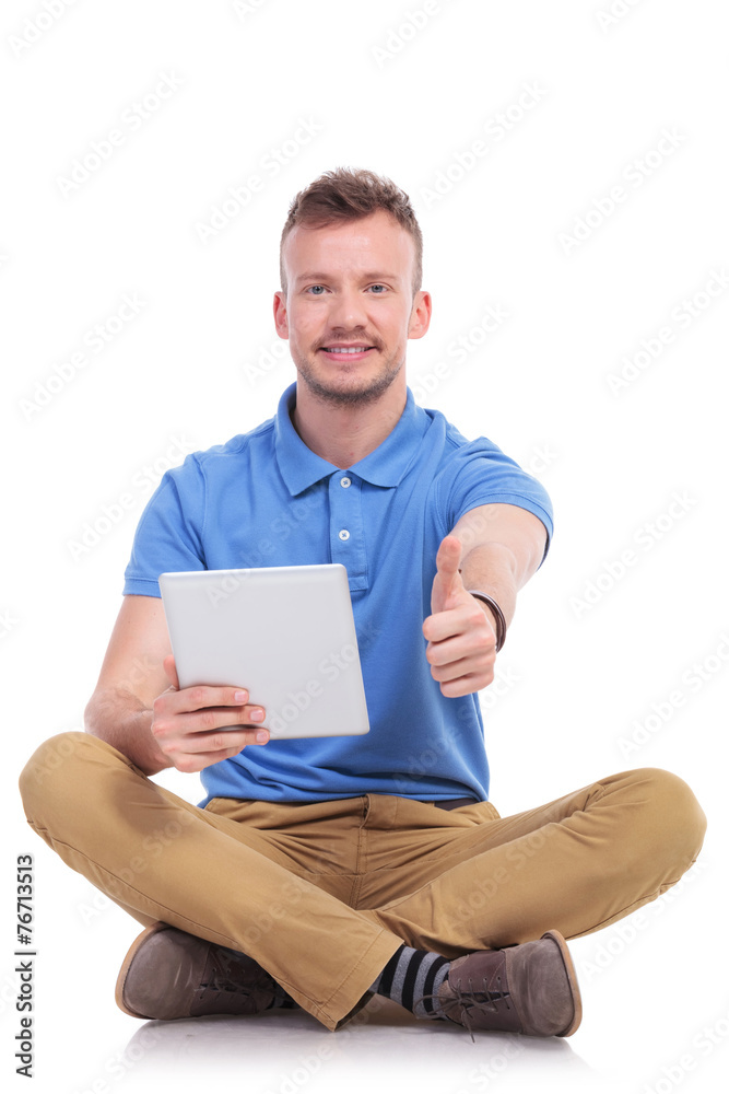 casual seated young man with tablet shows thumb up casual seated young man with tablet shows thumb up