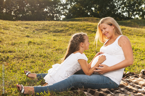 Happy little girl hugging her mother's pregnant belly