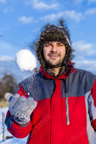 Handsome young man wearing cap and gloves playing with a snowbal photo