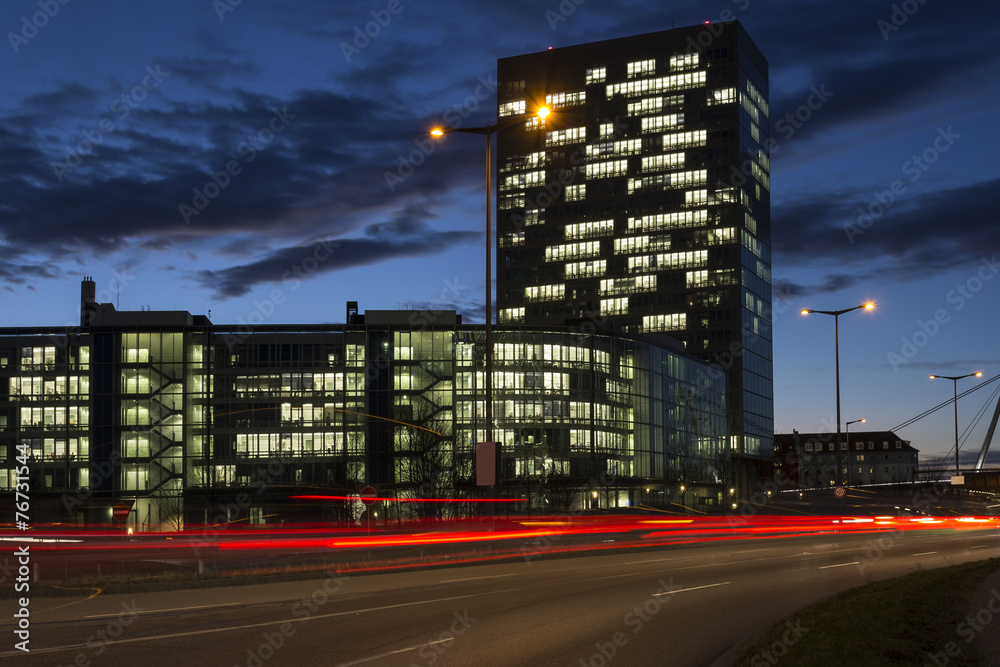 Befahrene Straße in München mit Bürogebäude bei Nacht