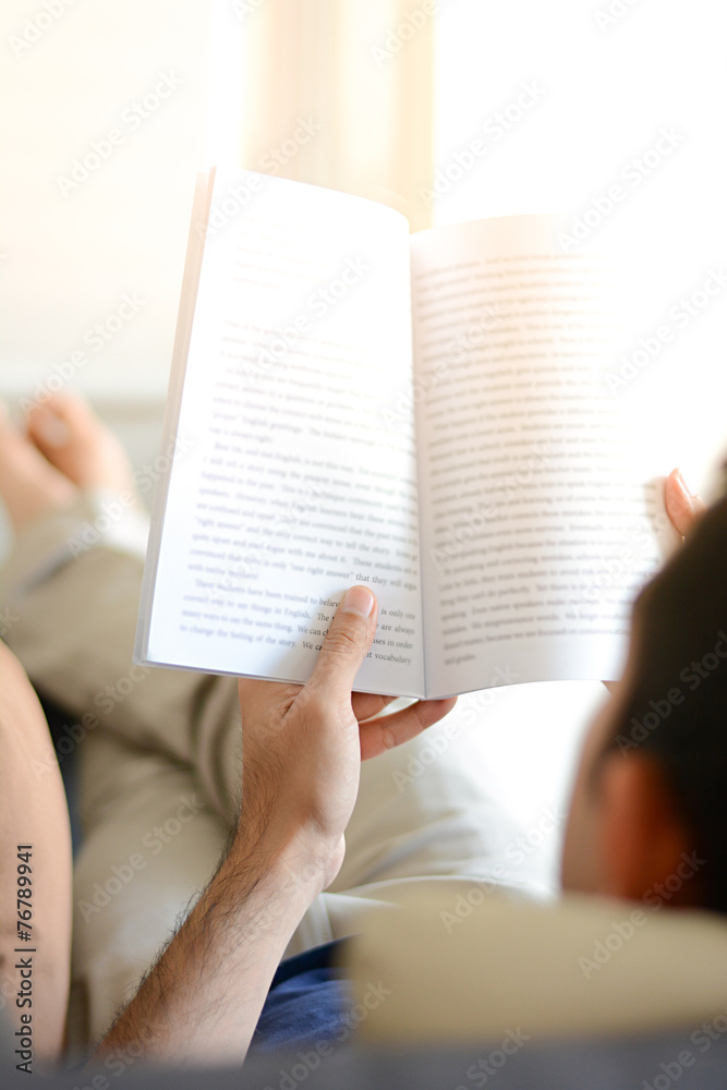 Naklejka premium A man reading book while lying on the couch