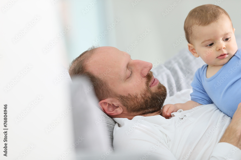 Father with baby boy relaxing in sofa at home
