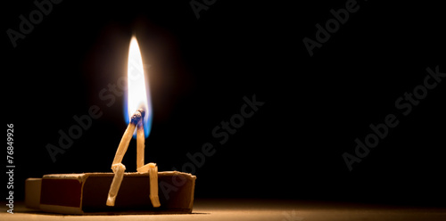 two matches burning sitting together on the matchbox in the dark