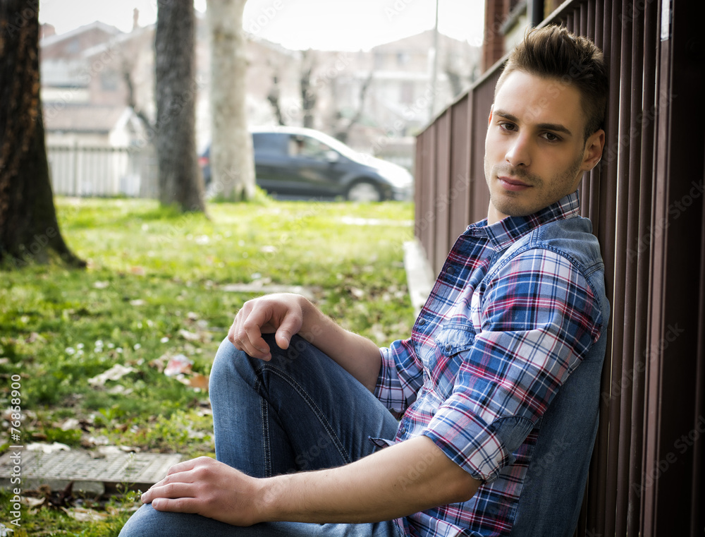 Fototapeta premium Profile of young man sitting on ground outdoors