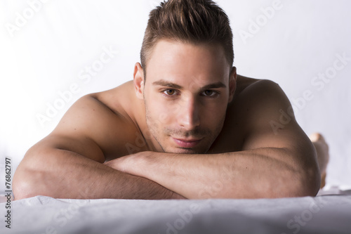 Cute expression, naked young man on white sheets