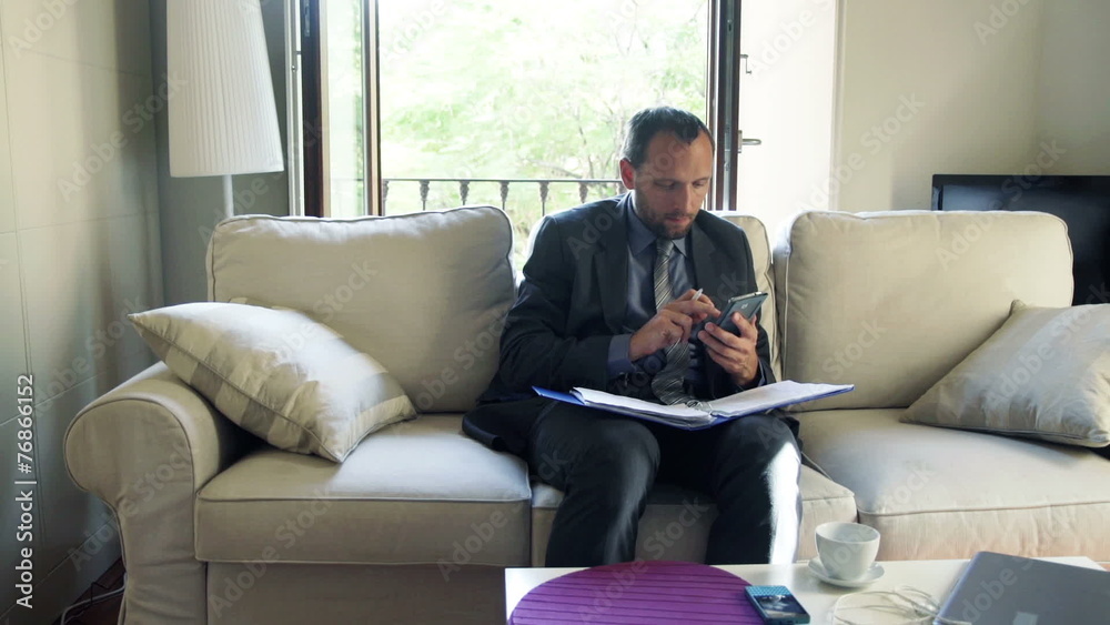 Businessman working with documents, smartphone sitting on sofa Businessman working with documents, smartphone sitting on sofa