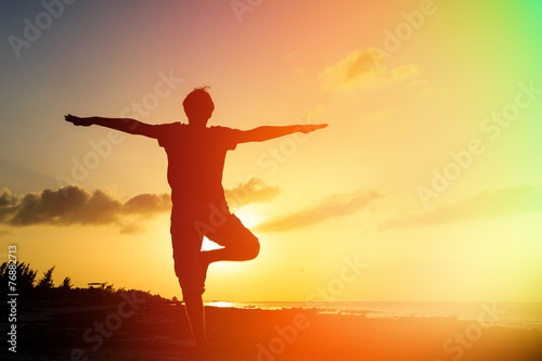 Silhouette of young man doing yoga at sunset