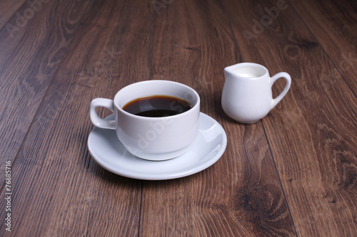 Кружка с чёрным кофе и молочник на деревянном столе