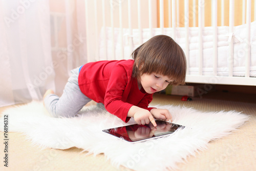 lovely 2 years boy in red shirt with tablet computer at home