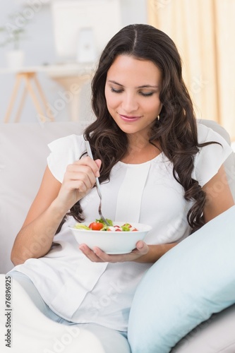 Pretty brunette eating salad on couch