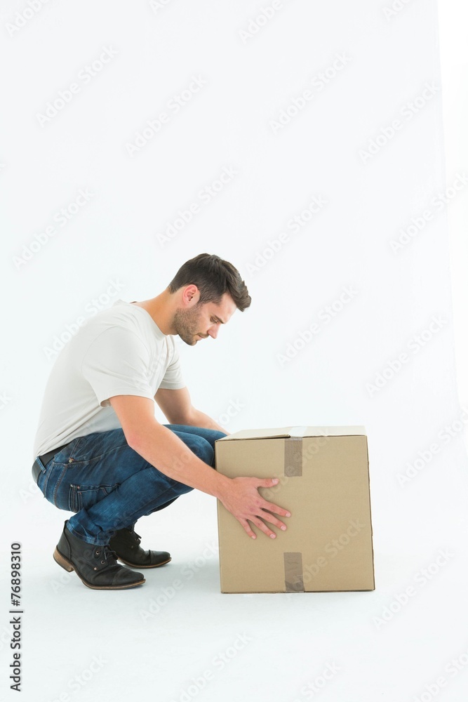 Delivery man crouching while picking cardboard box Delivery man crouching while picking cardboard box