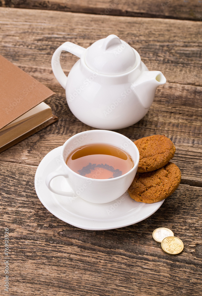 Image of ivory tea cup with sweet cookie, kettle and money on wo