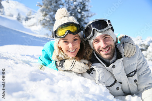 Cheerful couple of skiers laying down in snow