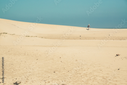 Bright sand dunes with male hiker on the horizon. Clear blue sky