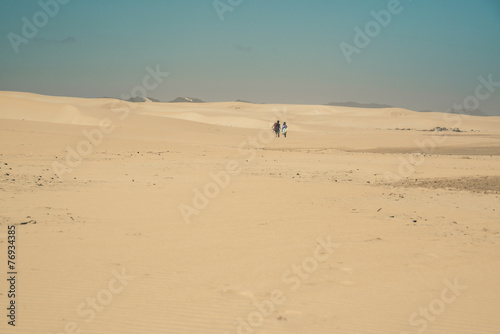Sand dune landscape with couple walking to the horizon. Clear bl