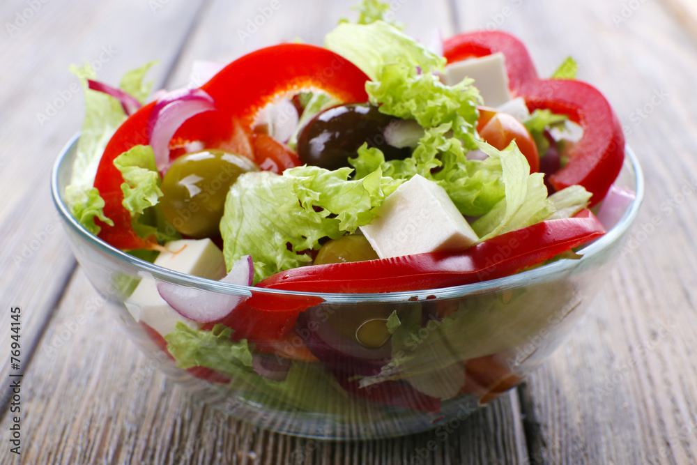Greek salad in glass dish on wooden table background Greek salad in glass dish on wooden table background