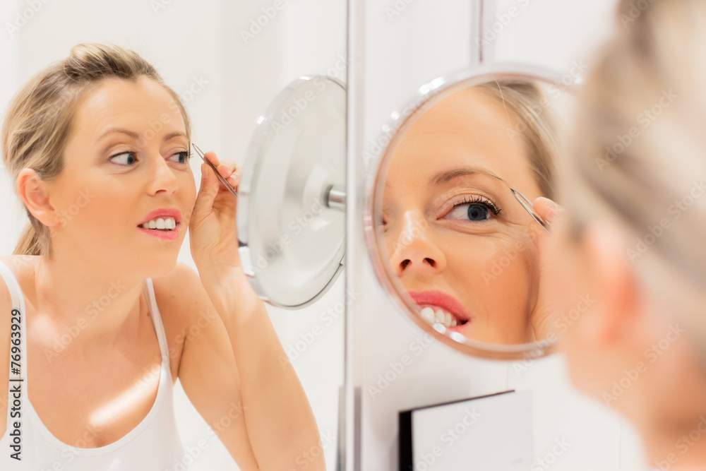 Young woman tweezing eyebrows in bathroom Young woman tweezing eyebrows in bathroom