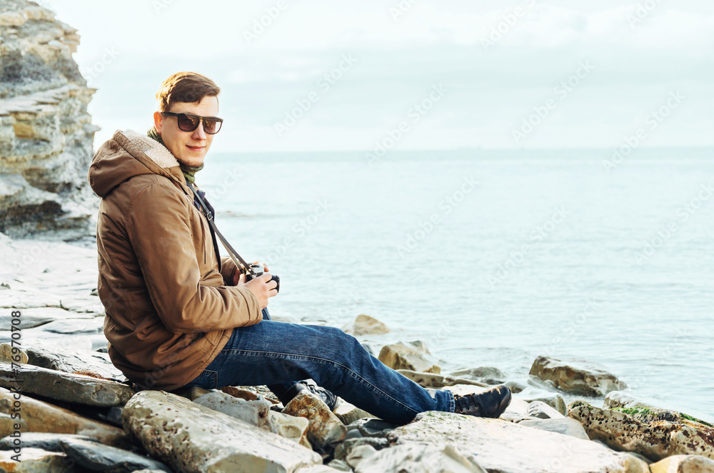 Man sitting on coastline with photo camera