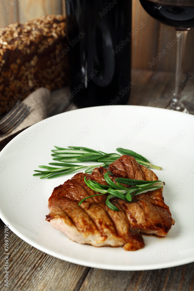 Steak with herbs on plate and bottle of wine on wooden table