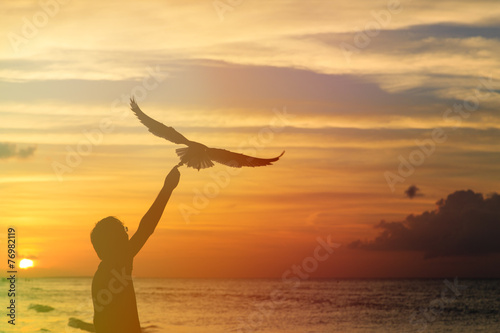 silhouette of man feeding seagull at sunset