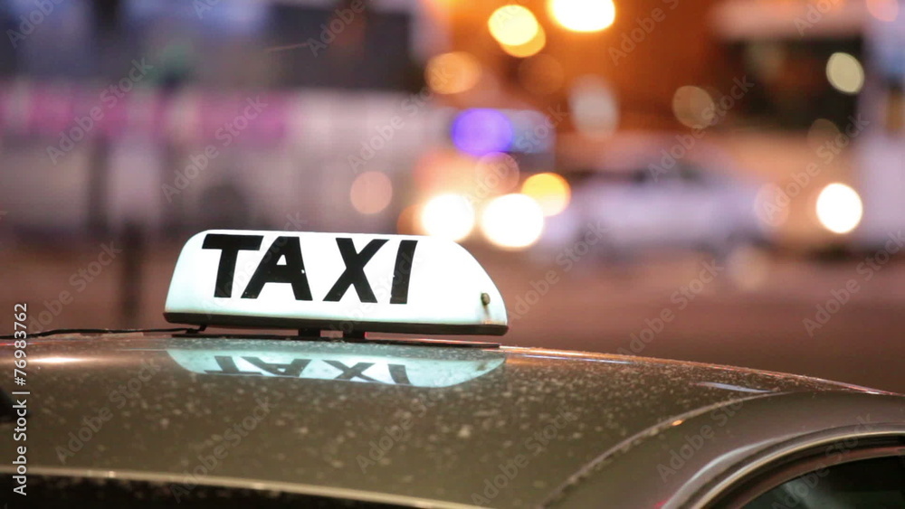 Shining Taxi inscription against passing cars on night street 