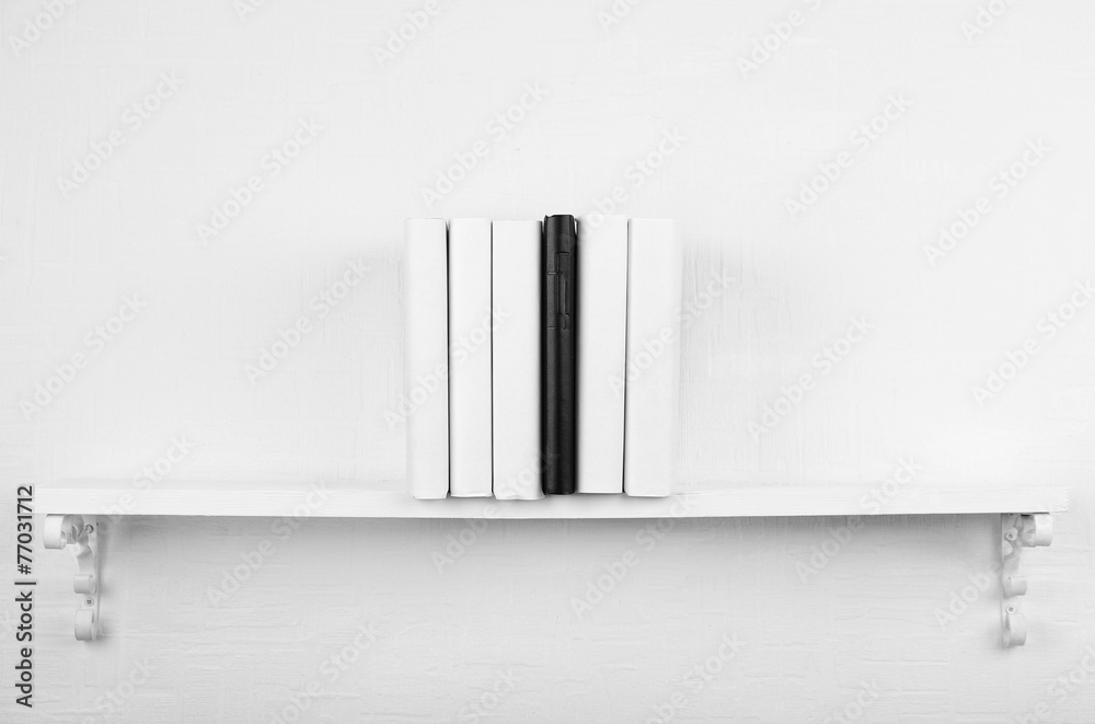 Blank books with black one on bookshelf on white wall Blank books with black one on bookshelf on white wall