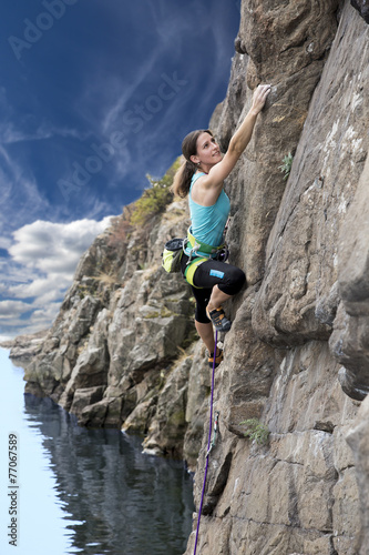 Female extreme climber conquers steep rock over rocky beach