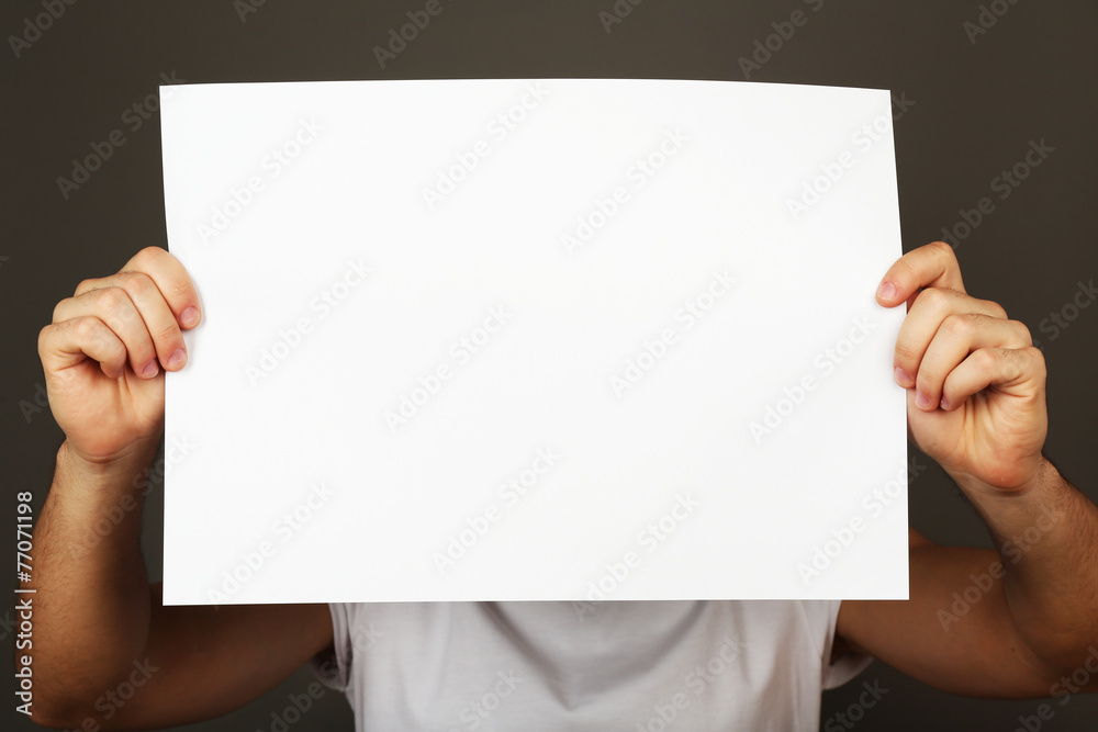 Blank sheet of paper in male hand on dark background Blank sheet of paper in male hand on dark background