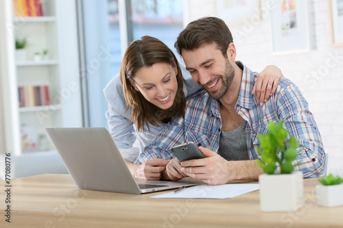 Couple at home using smartphone in front of laptop