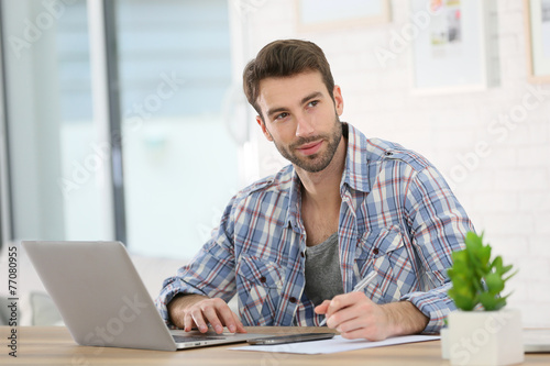 Man working from home with laptop and taking notes