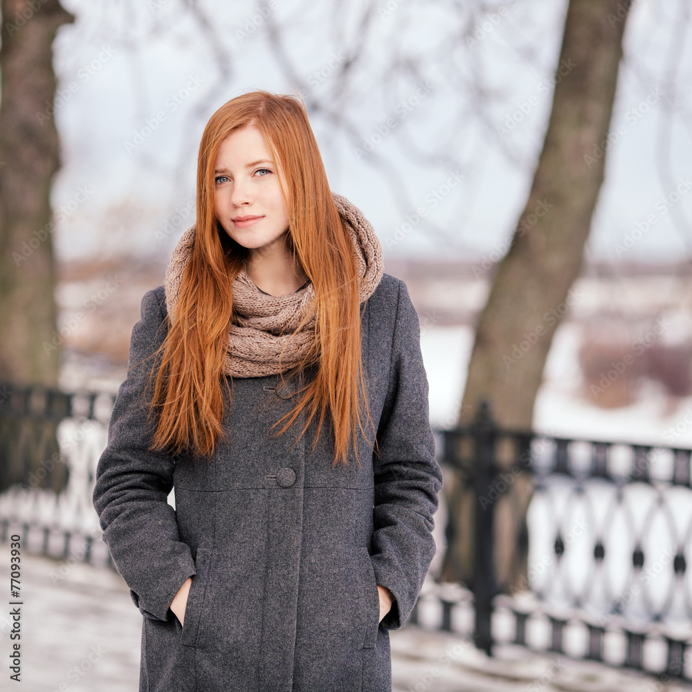 Beautiful redhead woman in grey coat strolling in winter park