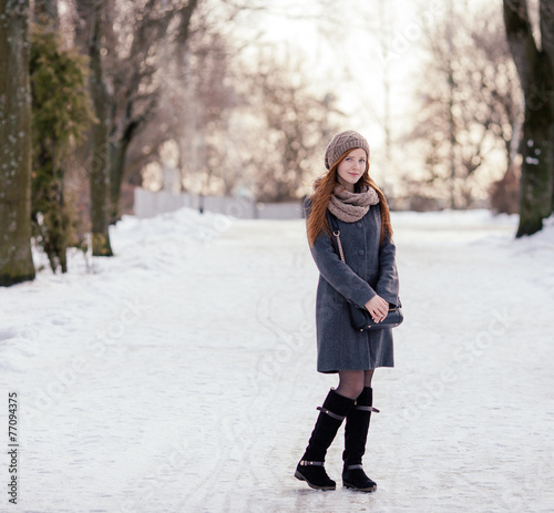 Beautiful redhead woman in grey coat strolling in winter park