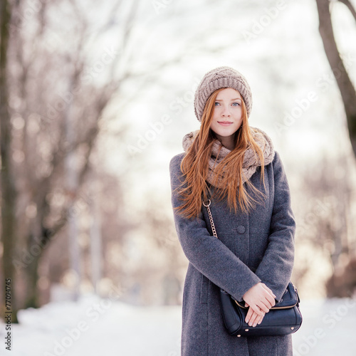 Beautiful redhead woman in grey coat strolling in winter park