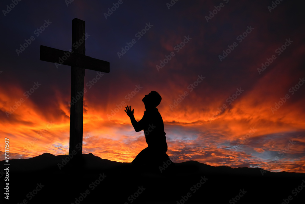 Naklejka premium Silhouette of man praying to a cross with heavenly cloudscape su