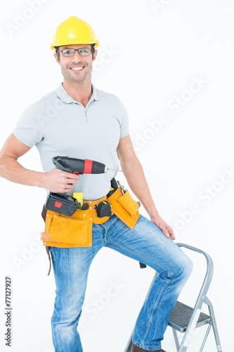 Worker holding drill machine on step ladder