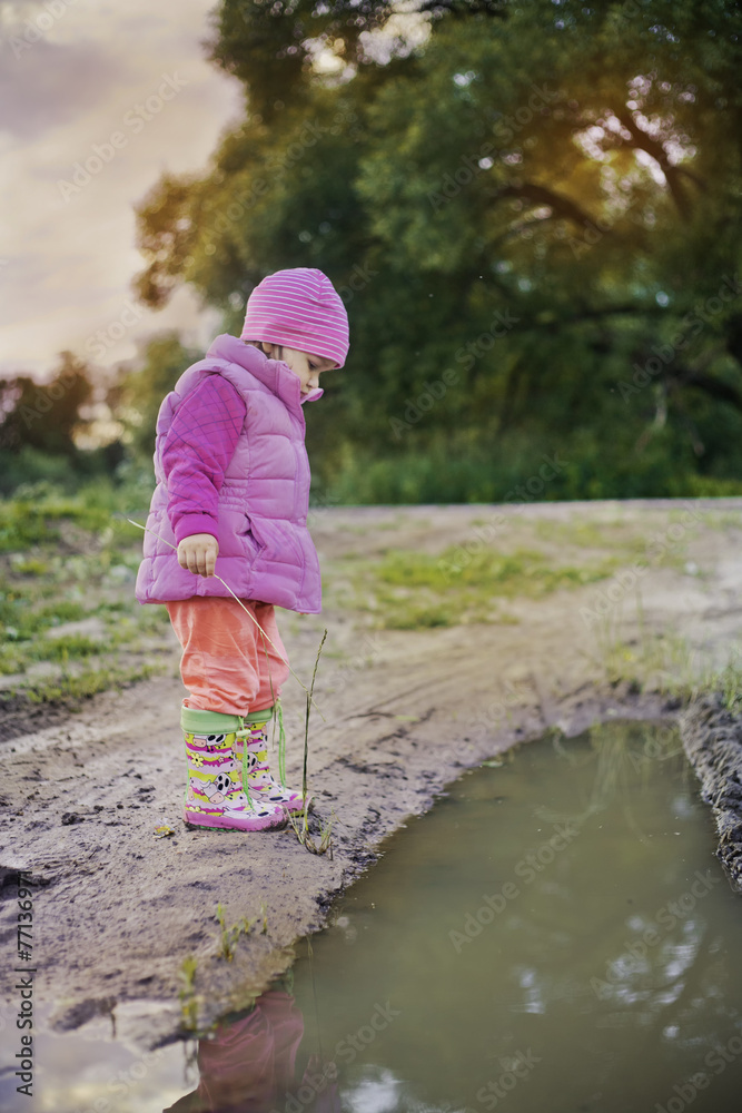 Cute little girl standing near a puddle at summer evening