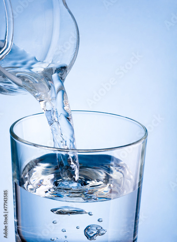 Close-up pouring water from a jug into glass on a blue backgroun
