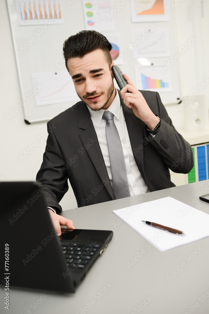 Fototapeta premium young businessman in office working on laptop computer and phone
