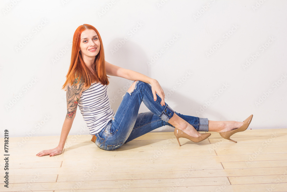 Smiling beautiful redhead woman with tattoo sitting on the floor Smiling beautiful redhead woman with tattoo sitting on the floor