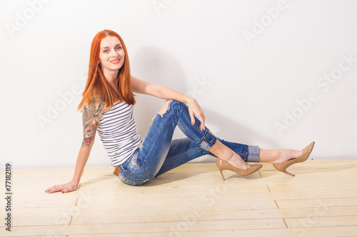 Smiling beautiful redhead woman with tattoo sitting on the floor