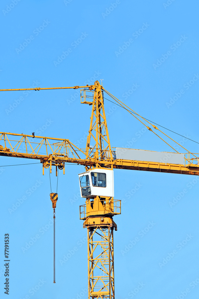 Yellow construction tower crane against blue sky Yellow construction tower crane against blue sky