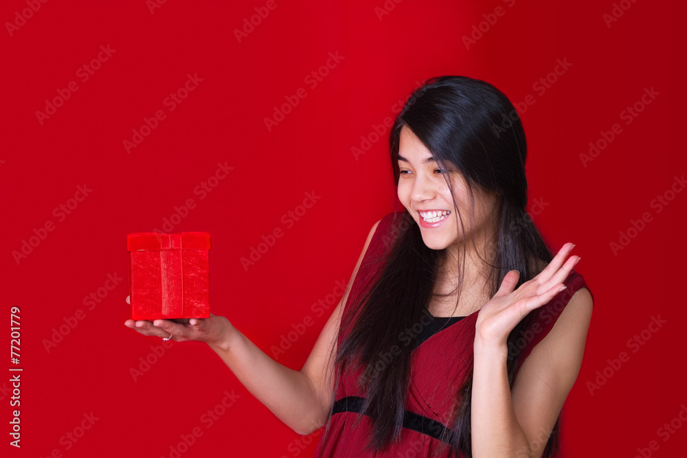 Beautiful biracial teen girl in red dress holding red present on Beautiful biracial teen girl in red dress holding red present on