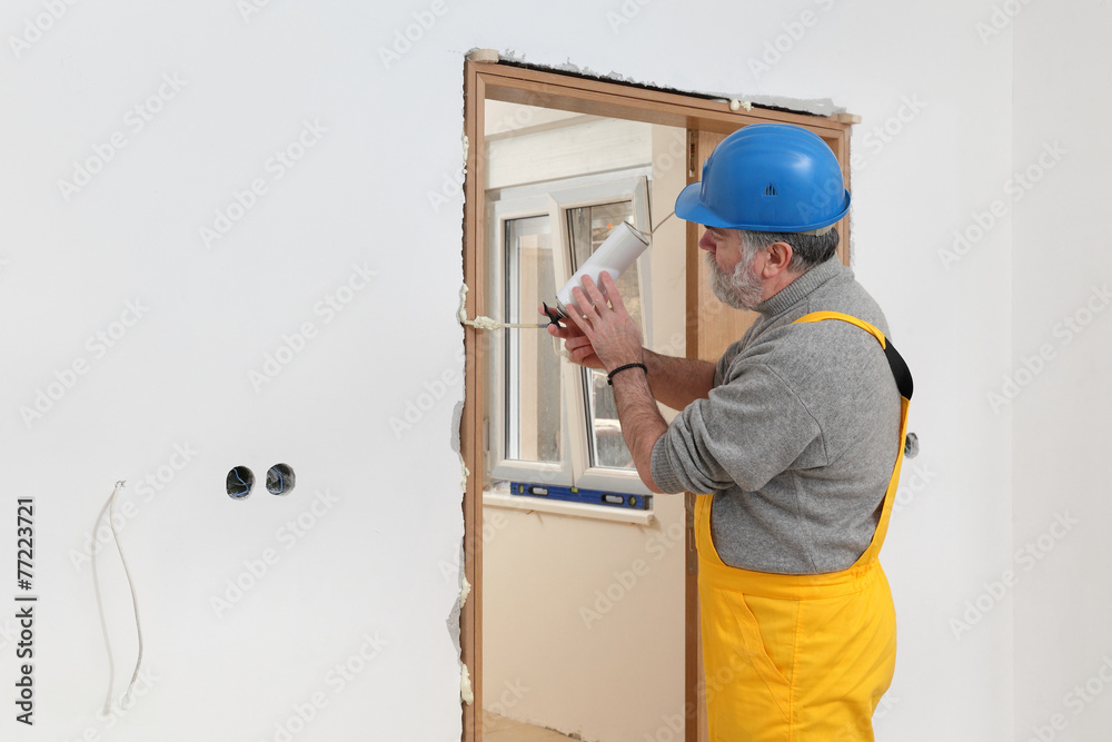Worker installing wooden door, using polyurethane foam Worker installing wooden door, using polyurethane foam