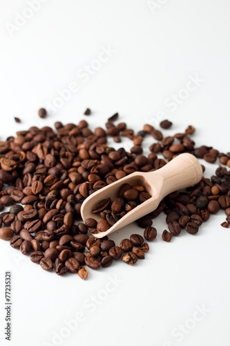 Heap of coffee grains on white board with wooden spoon