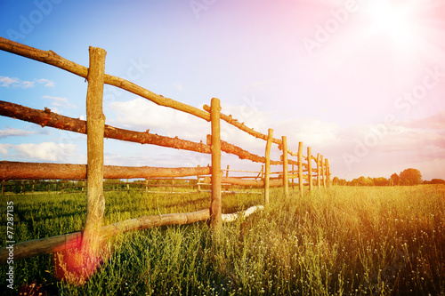 Fence in the green field under blue cloud sky